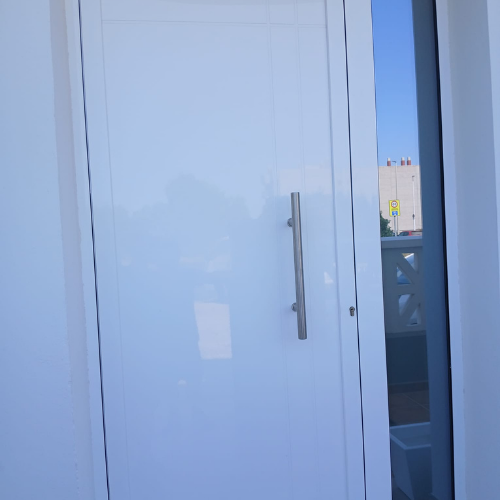 Puerta de entrada en aluminio blanco con panel liso y tirador vertical moderno.