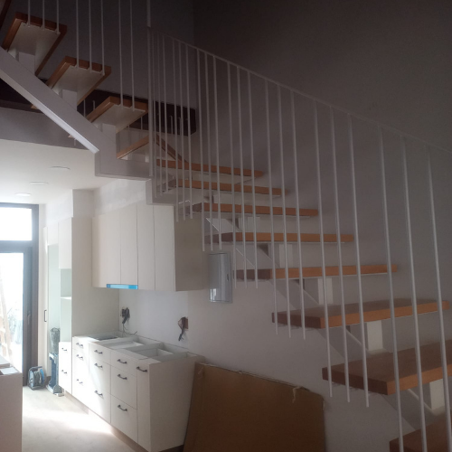 Escalera interior de diseño minimalista con estructura metálica blanca, peldaños de madera y barandilla vertical continua.