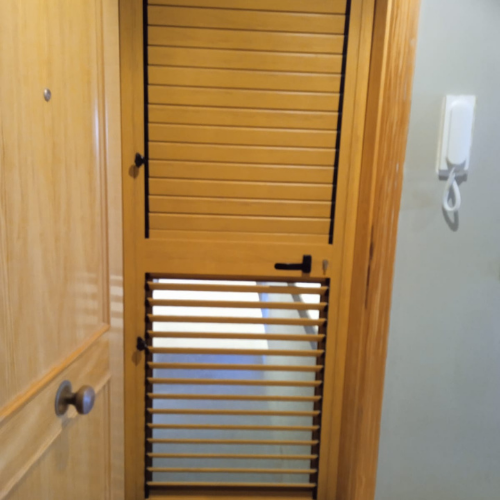 Puerta metálica en acabado madera con lamas superiores y panel inferior, ideal para acceso a exteriores o patios.