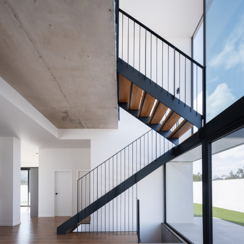 Barandilla interior en hierro lacado negro junto a escalera metálica con peldaños de madera en vivienda unifamiliar.