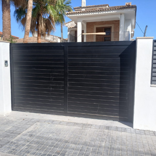 Puerta corredera metálica de gran formato con lamas horizontales y acabado negro mate para acceso a garaje de vivienda unifamiliar.