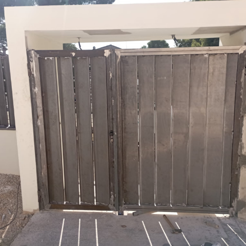 Puerta metálica de dos hojas montada en obra antes del acabado final, estructura en proceso de ajuste.