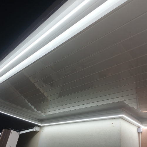 Detalle de lamas cerradas de pérgola bioclimática con iluminación LED integrada en estructura de aluminio blanco.