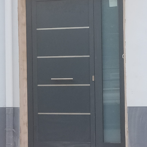 Puerta de acceso a vivienda en aluminio gris antracita con panel liso y líneas decorativas en acero.