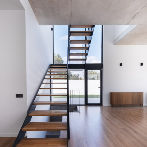 Escalera metálica de diseño minimalista con peldaños de madera en doble altura dentro de vivienda moderna.