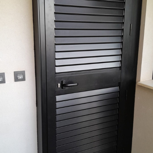 Puerta metálica negra con lamas horizontales para ventilación, ideal para interiores o accesos a cuartos técnicos.